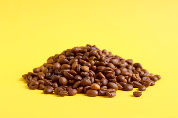 There is a small pile of coffee beans on a yellow background.