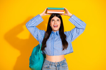 Trendy young woman balancing books on head with bright yellow background and cheerful expression