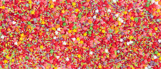 Colorful sugar candies sprinkle the background. Easter concept. Flat lay, top view, banner.