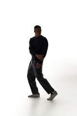 A young man strikes a dramatic pose, showcasing his style and confidence in a bright space.