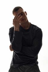 A handsome young man stands thoughtfully in a minimalist studio, conveying deep emotions.