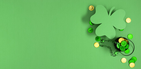 Festive green background banner decorated with gold and green coins, decorative pot, clover is perfect for celebrating St. Patrick's Day. Top view