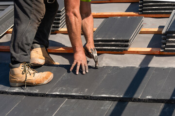 Close-up of Construction worker installing roofing tiles on a sunny day at a residential site