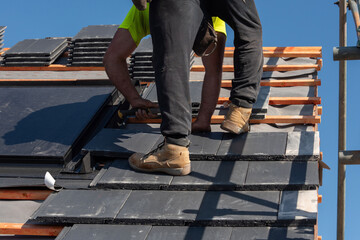 Roofing worker installs slate tiles on a construction site under clear blue sky on bright sunny day