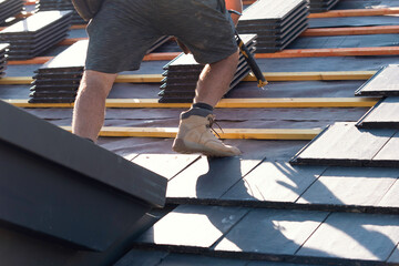 Worker installing slate roofing tiles on a sunny day in a residential area © Iryna