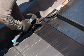 Skilled worker repairing roofing material with hammer and special tools on a sunny day
