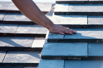 Close-up of Roofing project showcasing hand placement on slate tiles under clear sky