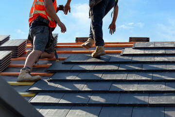Roofers install slate tiles on a sunny day at a construction site in a suburban area