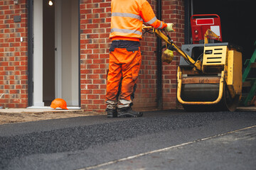 Construction worker applying asphalt in residential area private parking spot driveway