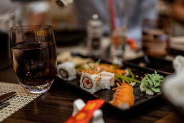 Close-up of sushi platter with rolls, salmon, wasabi, and a glass of wine on a table setting in a dimly lit restaurant ambiance..