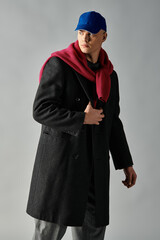 A young man with a handsome appearance wears a stylish coat and cap, showcasing confident fashion.