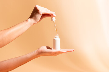 Female hands hold white serum bottle. Beauty routine.