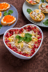 Salad with chicken, pineapple and pomegranate in a heart-shaped salad bowl next to tartlets