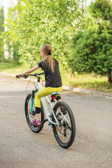 Obraz premium Preteen girl riding bicycle along tree-lined path during sunny weather