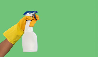 Hand holding a spray bottle with yellow glove against a green background for cleaning tasks