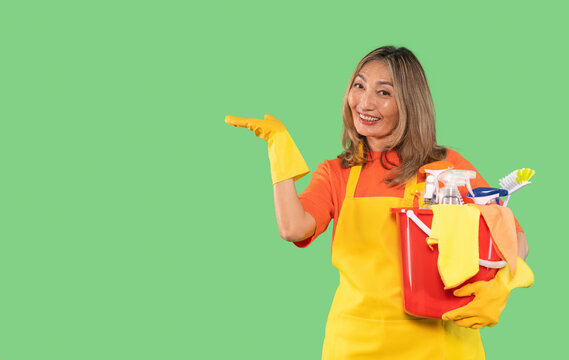 Woman wearing gloves holding cleaning supplies with a smile against a green background