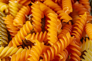 A colorful close-up of dry spiral pasta in vibrant orange, yellow, and green hues, highlighting its...