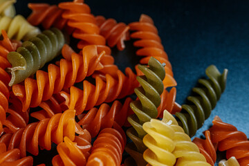 A colorful close-up of dry spiral pasta in vibrant orange, yellow, and green hues, highlighting its...