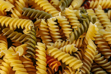 A colorful close-up of dry spiral pasta in vibrant orange, yellow, and green hues, highlighting its...