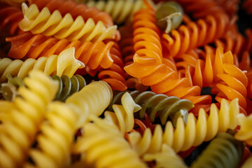 A colorful close-up of dry spiral pasta in vibrant orange, yellow, and green hues, highlighting its...