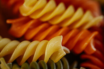 A colorful close-up of dry spiral pasta in vibrant orange, yellow, and green hues, highlighting its...