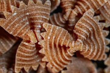 Close-up of dry bow-tie-shaped pasta with a ridged texture. The intricate patterns highlight its unique design, making it ideal for culinary-themed visuals and food concepts.