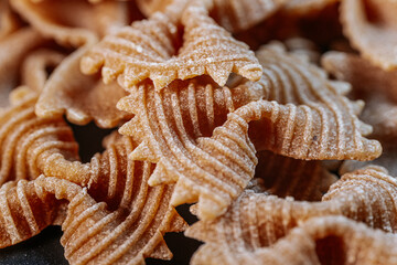 Close-up of dry bow-tie-shaped pasta with a ridged texture. The intricate patterns highlight its...