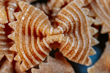 Close-up of dry bow-tie-shaped pasta with a ridged texture. The intricate patterns highlight its...