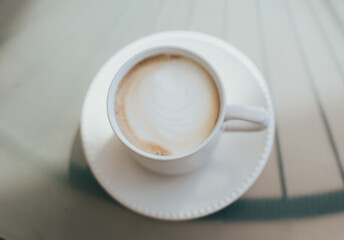 Delicious cappuccino coffee served in a white cup on a glass table.
