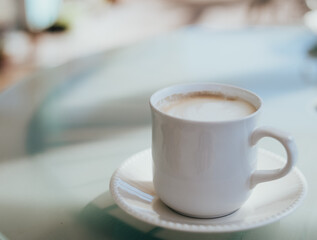 Delicious cappuccino coffee served in a white cup on a glass table.