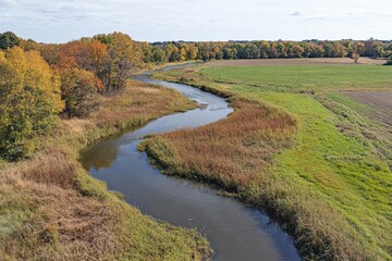 Serene Autumn Landscape with Meandering River Reflecting Colorful Foliage and Lush Green Fields in Rural Setting Under a Clear Blue Sky