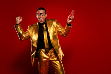 Charismatic young man in a shiny golden suit celebrating with a smartphone.