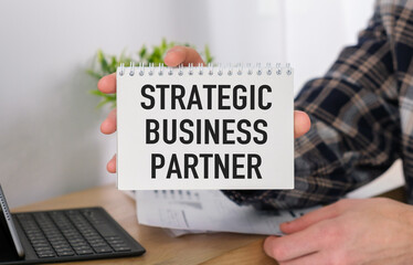Businessman putting a card with text STRATEGIC BUSINESS PARTNER in the office table
