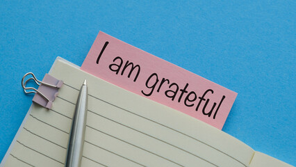 Note paper on blue background with handwritten text I AM GRATEFUL - concept of gratitude , means being thankful or show appreciation for good things or kindness in life