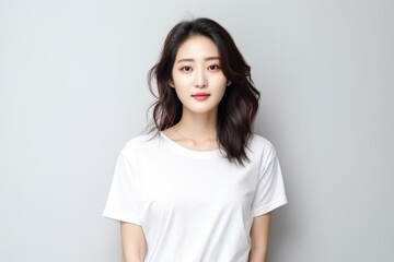 Obraz premium Studio shot of a beautiful young asian woman wearing a white t shirt, posing against a gray background