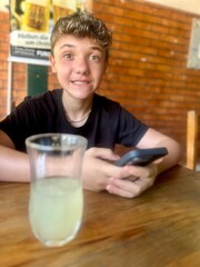 Pretty Blond boy, Smiling  in restaurant, with blue clothes, with glass and Cell phone