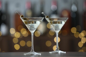Martini cocktail with olives in glasses on wooden table against blurred background, closeup. Bokeh effect