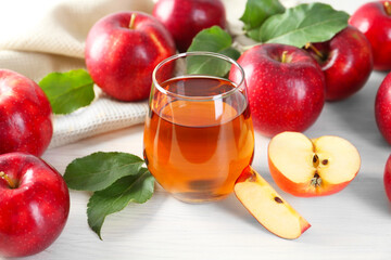 Fresh apple juice in glass, fruits and green leaves on white wooden table