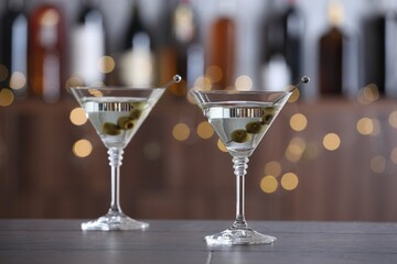 Martini cocktail with olives in glasses on wooden table against blurred background. Bokeh effect