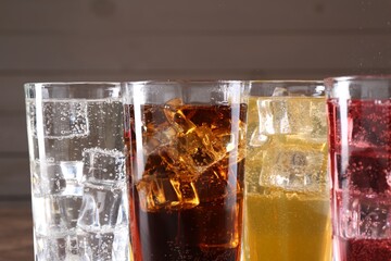 Refreshing soda water of different flavors with ice cubes in glasses on blurred background, closeup