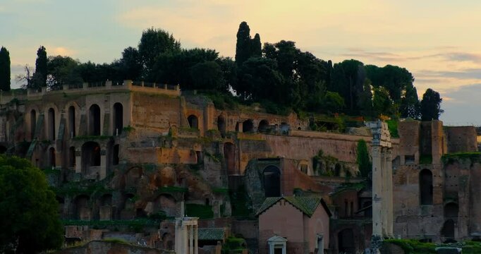 Sunset color view of Ancient Rome ruins with arched structures, weathered stone walls, and overgrown greenery. Iconic columns and remnants of Roman architecture evoke grandeur of Roman Empire Forum
