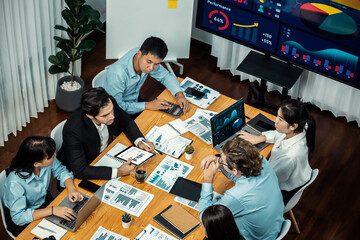 Wide top view of diverse group of business analyst team analyzing financial data report paper on meeting table. Chart and graph dashboard by business intelligence analysis. Meticulous