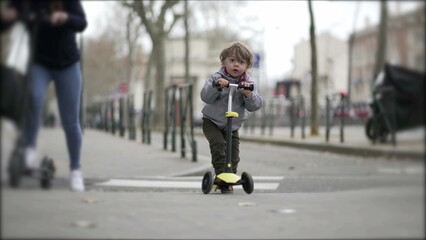 Toddler kid riding scooter in street