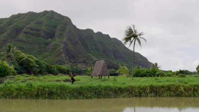 Blue haired warrior pretending to shoot gun around tropical area and nearly tripping - wide, side scrolling shot