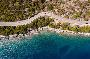 Aerial vertical shot of pickup cars moving by the curved road near sea tranquil waves on coast on...