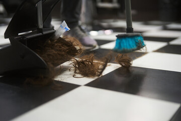 Cleaning hair on a checkered floor with a broom in a salon