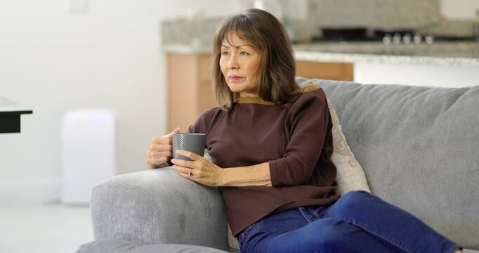 Woman enjoying relaxing sitting on home sofa drinking hot morning coffee looking around
