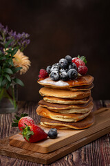 American pancakes with blueberries, strawberries and raspberry on a plate on a dark background
