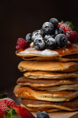 American pancakes with blueberries, strawberries and raspberry on a plate on a dark background