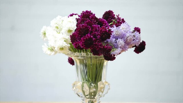 A vase filled with purple and white flowers. The flowers are arranged in a way that creates a sense of balance and harmony. The vase itself is clear and elegant